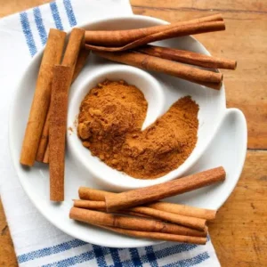 پودر دارچین قهوه‌ای رنگ در کنار چوب دارچین لوله‌ای با کیفیت بالا